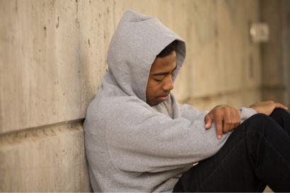 a young man in a hooded sweatshirt sitting against a wall - juvenile charges