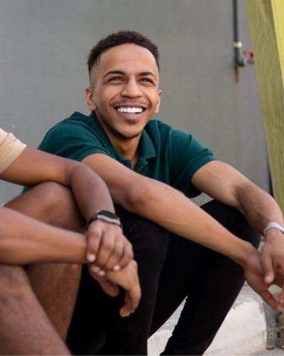 a man sitting on a curb outside with friends, smiling, after having his record expunged.